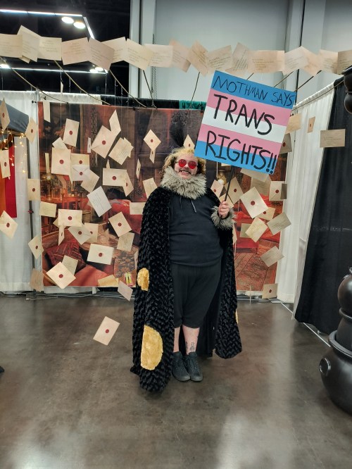 Mothman cosplayer holding a trans rights sign